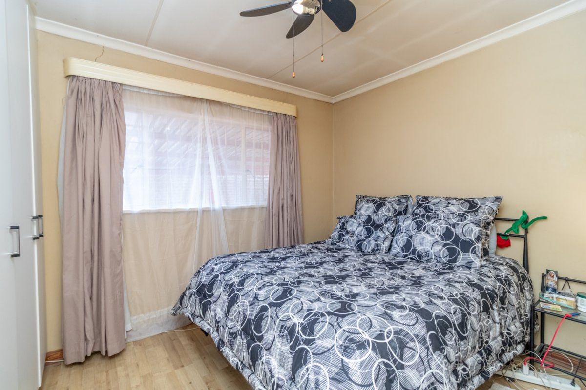 A bedroom featuring laminate flooring, a ceiling fan, and built-in wardrobe storage, showing signs of wear on the ceiling.