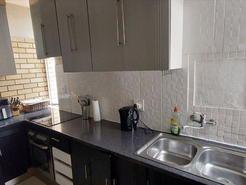 A functional kitchen featuring dark cabinetry, laminate countertops, a double bowl stainless steel sink, and a built-in oven with an electric hob.