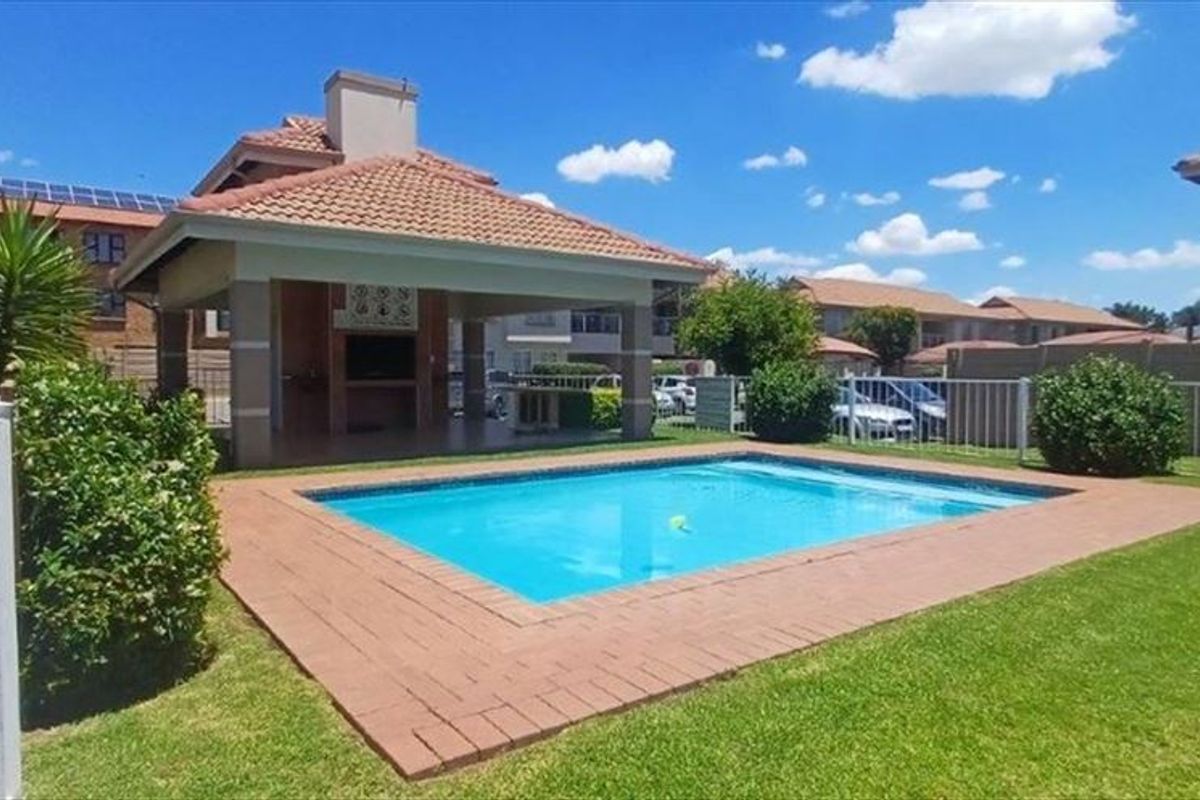 Communal outdoor area featuring a swimming pool, landscaped garden, and a covered patio with a built-in braai facility.