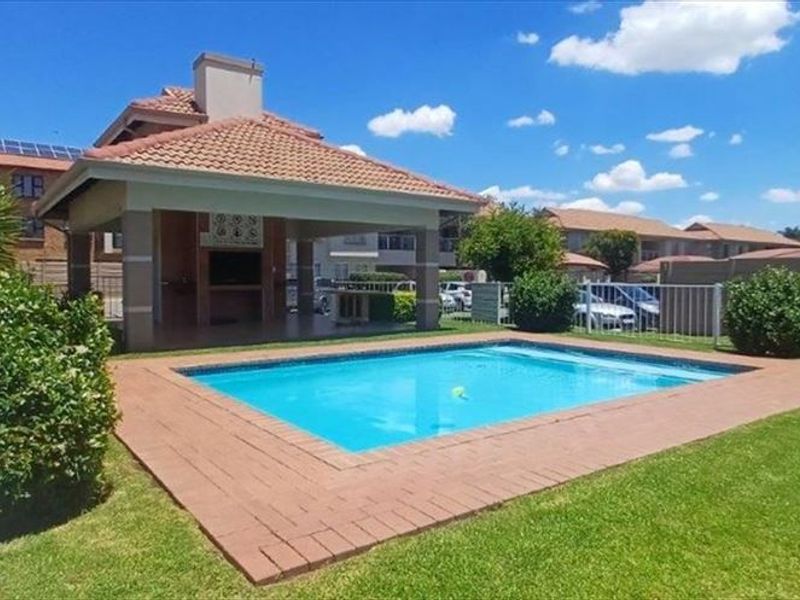 Communal outdoor area featuring a swimming pool, landscaped garden, and a covered patio with a built-in braai facility.