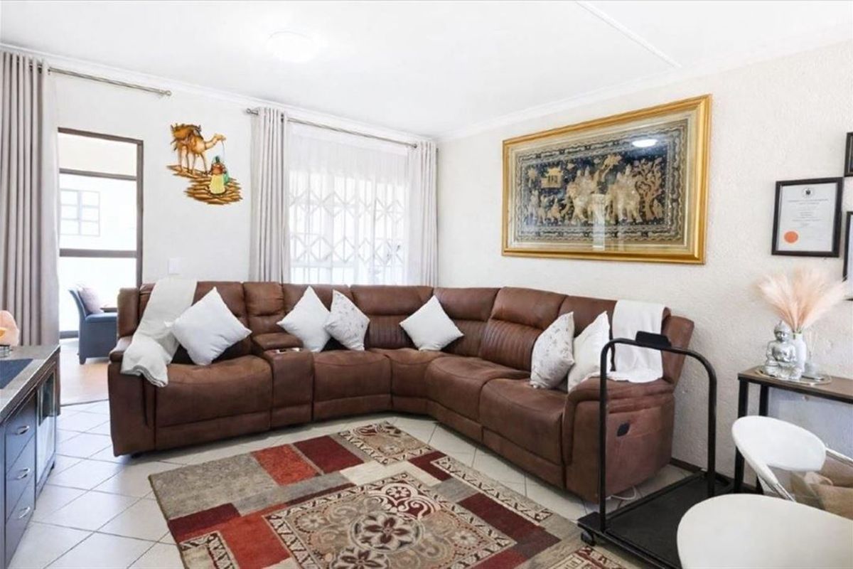 A comfortable living room featuring tiled flooring, a sliding door with security gate, and neutral wall finishes.