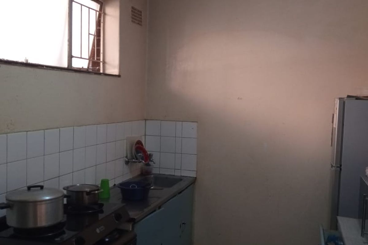 A functional kitchen area featuring a sink, tiled splashback, and built-in cabinetry, requiring cosmetic updates to improve its overall aesthetic and condition.