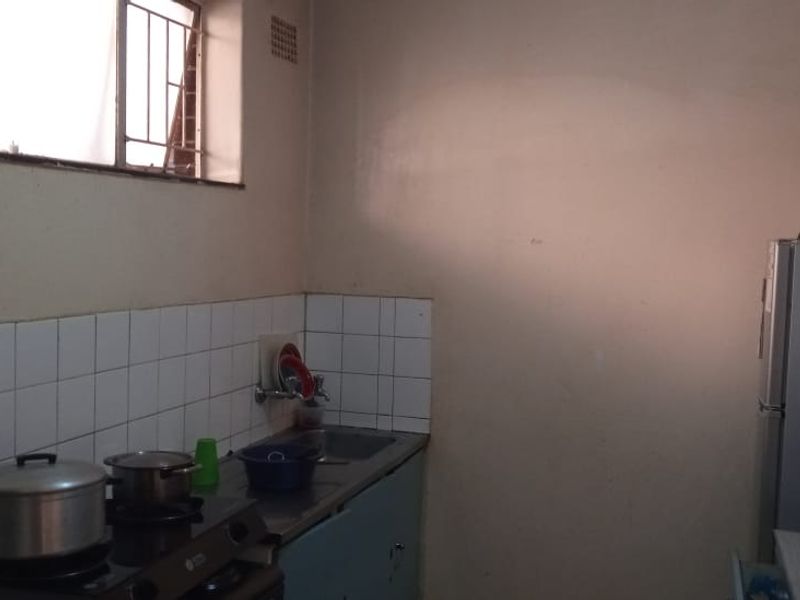 A functional kitchen area featuring a sink, tiled splashback, and built-in cabinetry, requiring cosmetic updates to improve its overall aesthetic and condition.