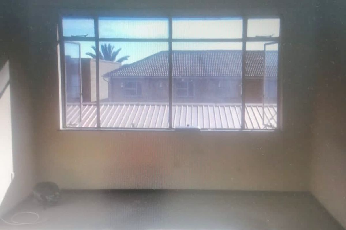 An empty bedroom featuring a large aluminium-framed window with views of the surrounding residential complex.