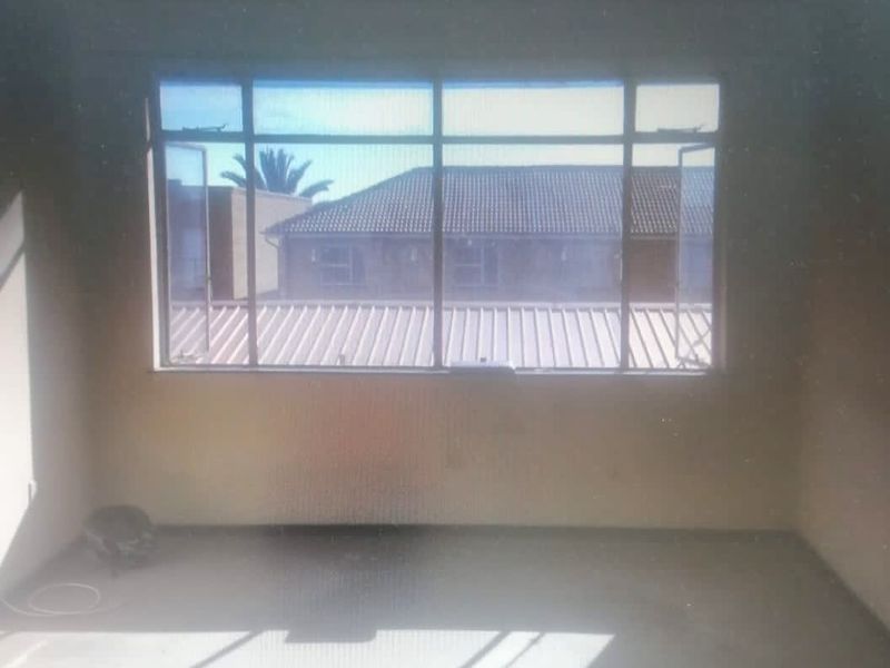 An empty bedroom featuring a large aluminium-framed window with views of the surrounding residential complex.