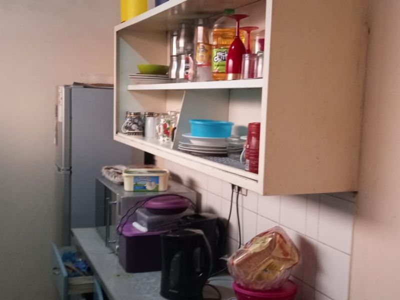 A compact kitchen area featuring wall-mounted cabinetry and a tiled splashback, requiring cosmetic updates to improve the overall aesthetic and functionality.