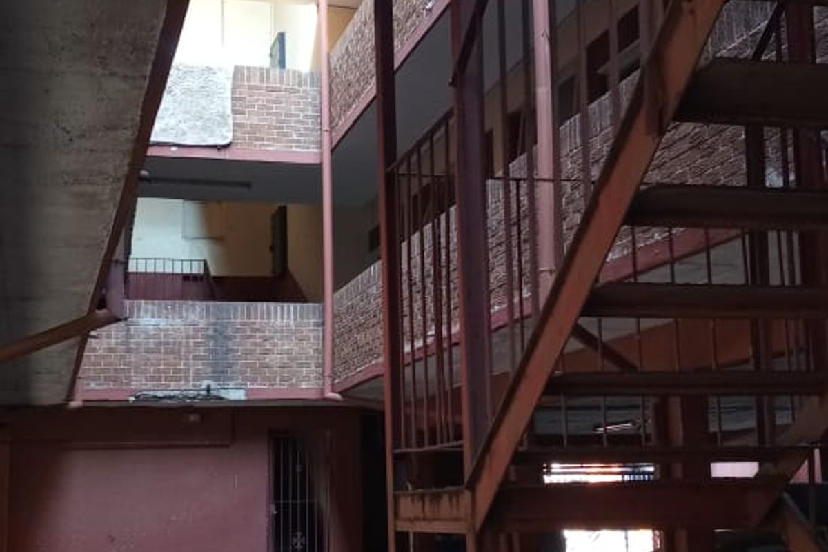 Exterior view of an apartment complex featuring a metal staircase, brick facade, and paved ground level parking area.