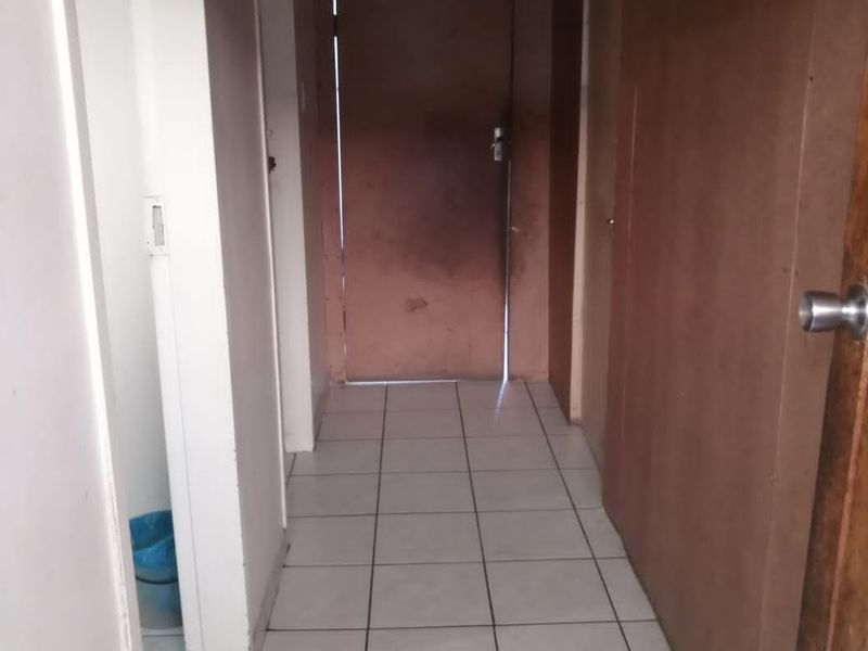 A narrow hallway featuring tiled flooring and multiple internal doors, requiring cosmetic updates to improve the overall aesthetic and lighting.