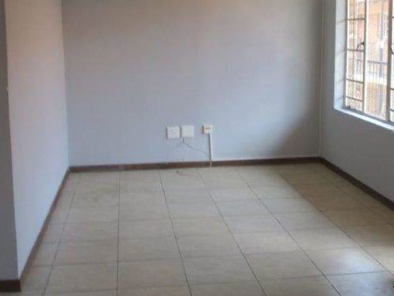 An empty bedroom featuring tiled flooring, a window with security bars, and a wooden door.
