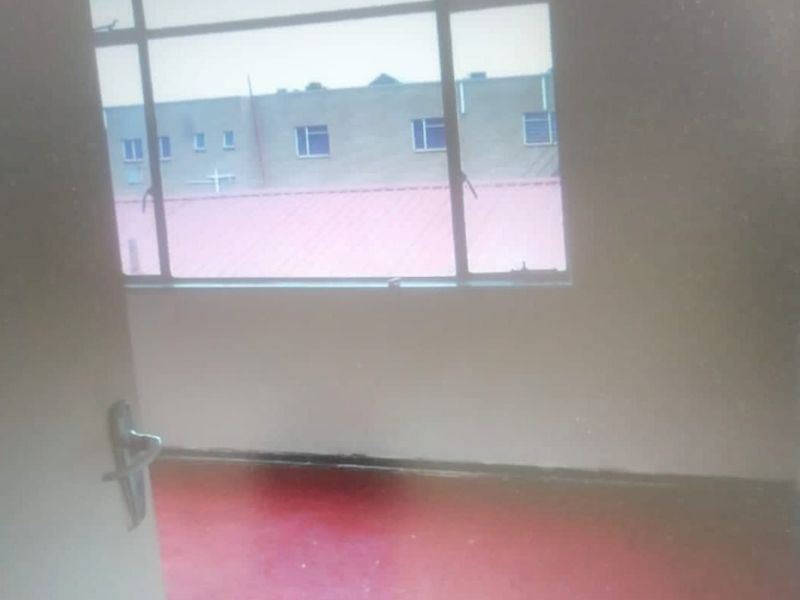 An empty bedroom featuring a metal-framed window and worn flooring, requiring cosmetic updates to improve its overall appeal.
