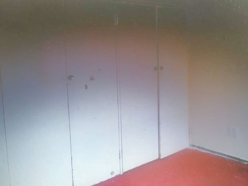 An empty bedroom featuring built-in cupboards and red carpeting, requiring cosmetic updates to improve the overall aesthetic and condition.