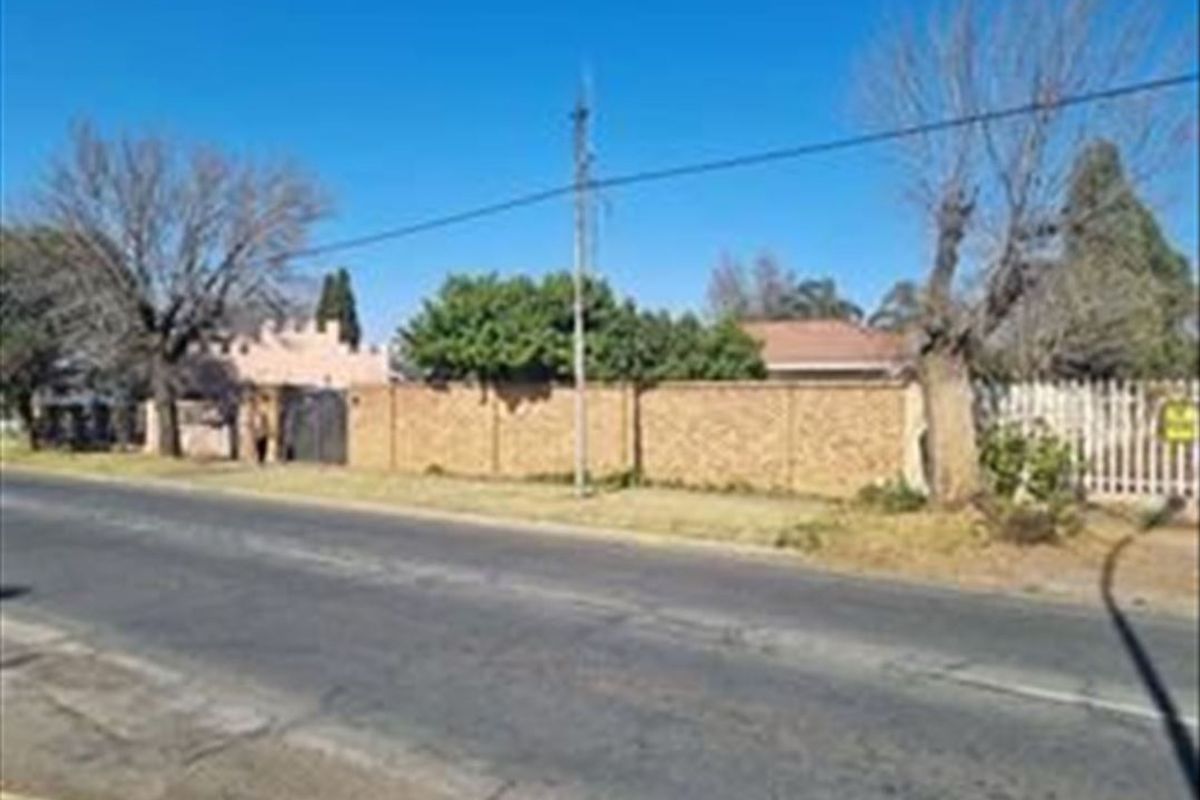 Street view of the property showing the brick boundary wall, utility pole, and surrounding mature trees along the roadside.