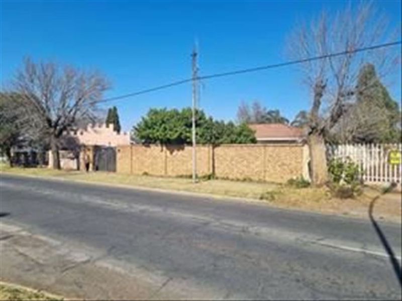 Street view of the property showing the brick boundary wall, utility pole, and surrounding mature trees along the roadside.