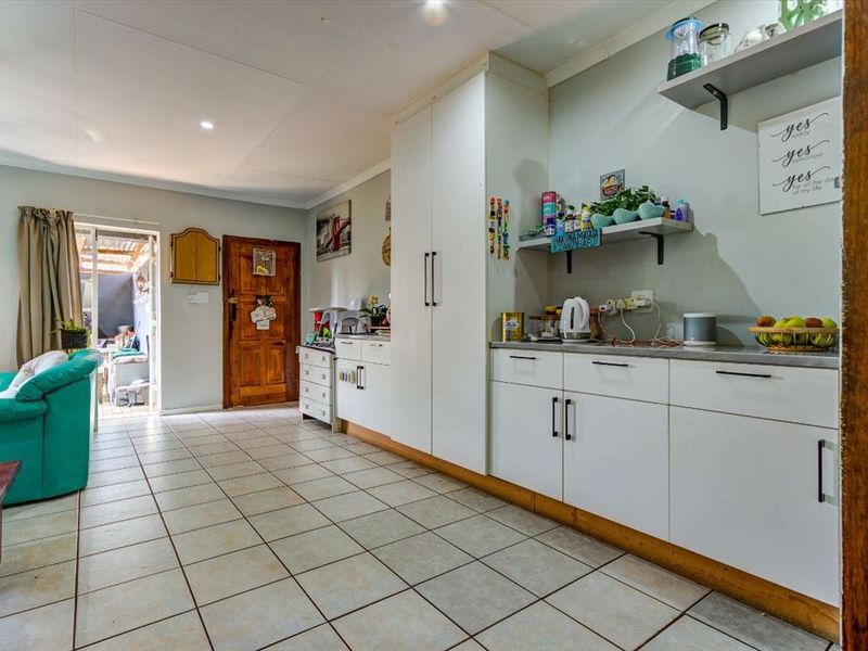 A functional kitchen area featuring white built-in cabinetry, laminate countertops, open shelving, and tiled flooring, with direct access to an outdoor patio space.