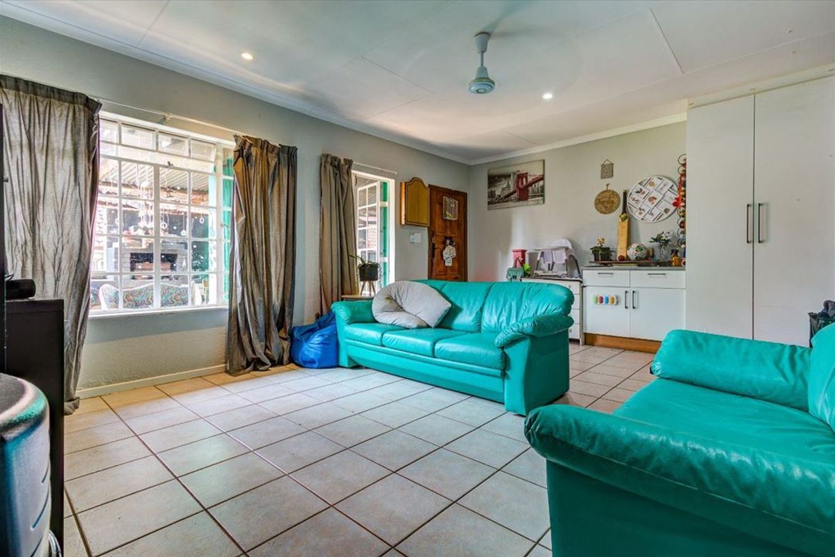 A spacious living room featuring tiled flooring, recessed lighting, a ceiling fan, and built-in storage cabinetry, with natural light from large windows.