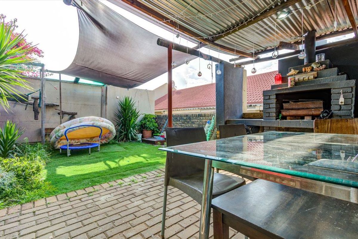 Covered outdoor patio area featuring a built-in brick braai, paved flooring, and a shade sail, providing a functional space for outdoor entertaining.