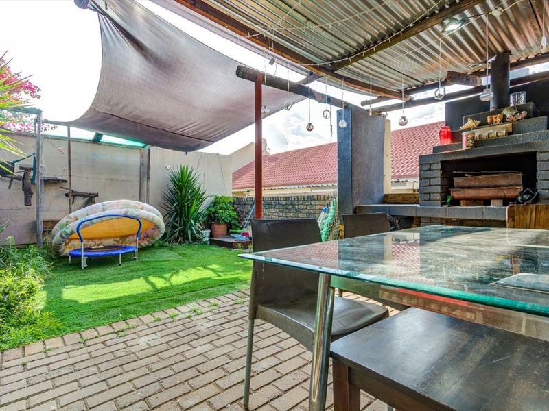 Covered outdoor patio area featuring a built-in brick braai, paved flooring, and a shade sail, providing a functional space for outdoor entertaining.