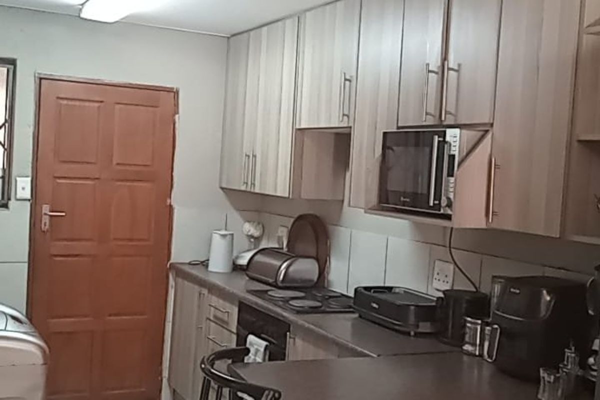 A functional kitchen featuring wood-look cabinetry, laminate countertops, built-in cooking appliances, and tiled flooring with direct access to an exterior door.
