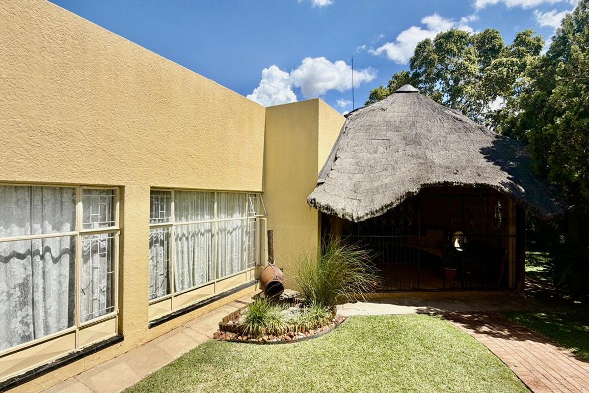 Rear exterior view featuring a lawn, brick pathway, and a traditional thatched lapa structure adjacent to the main house.
