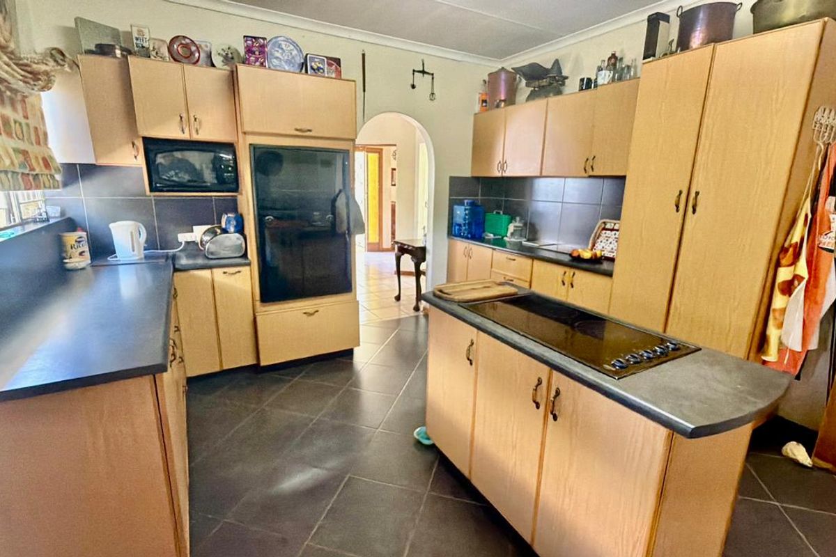 A functional kitchen featuring light wood-finish cabinetry, dark tiled flooring, a central island with a built-in cooktop, and a classic arched doorway.