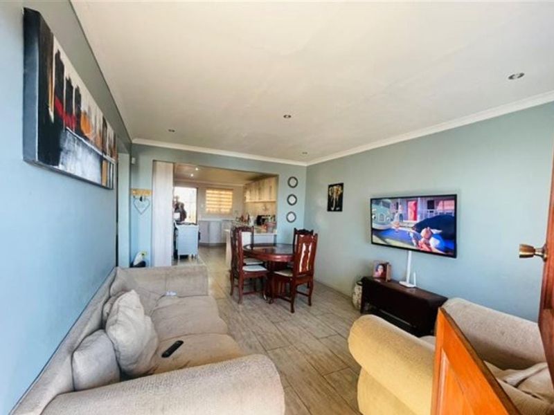 An open-plan living and dining area featuring tiled flooring, recessed lighting, and a wall-mounted television, flowing into the adjacent kitchen space.