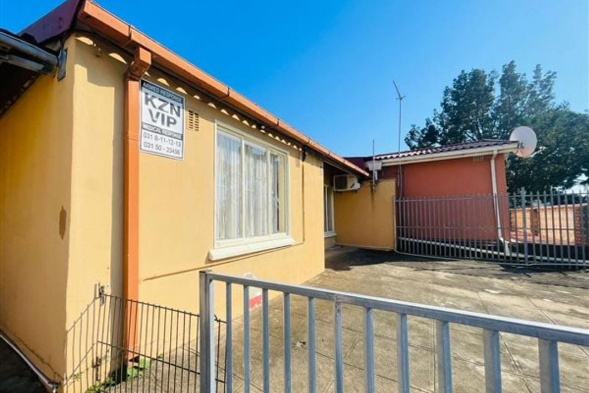 Rear exterior view of the property featuring a paved patio area, security fencing, and an external air conditioning unit.