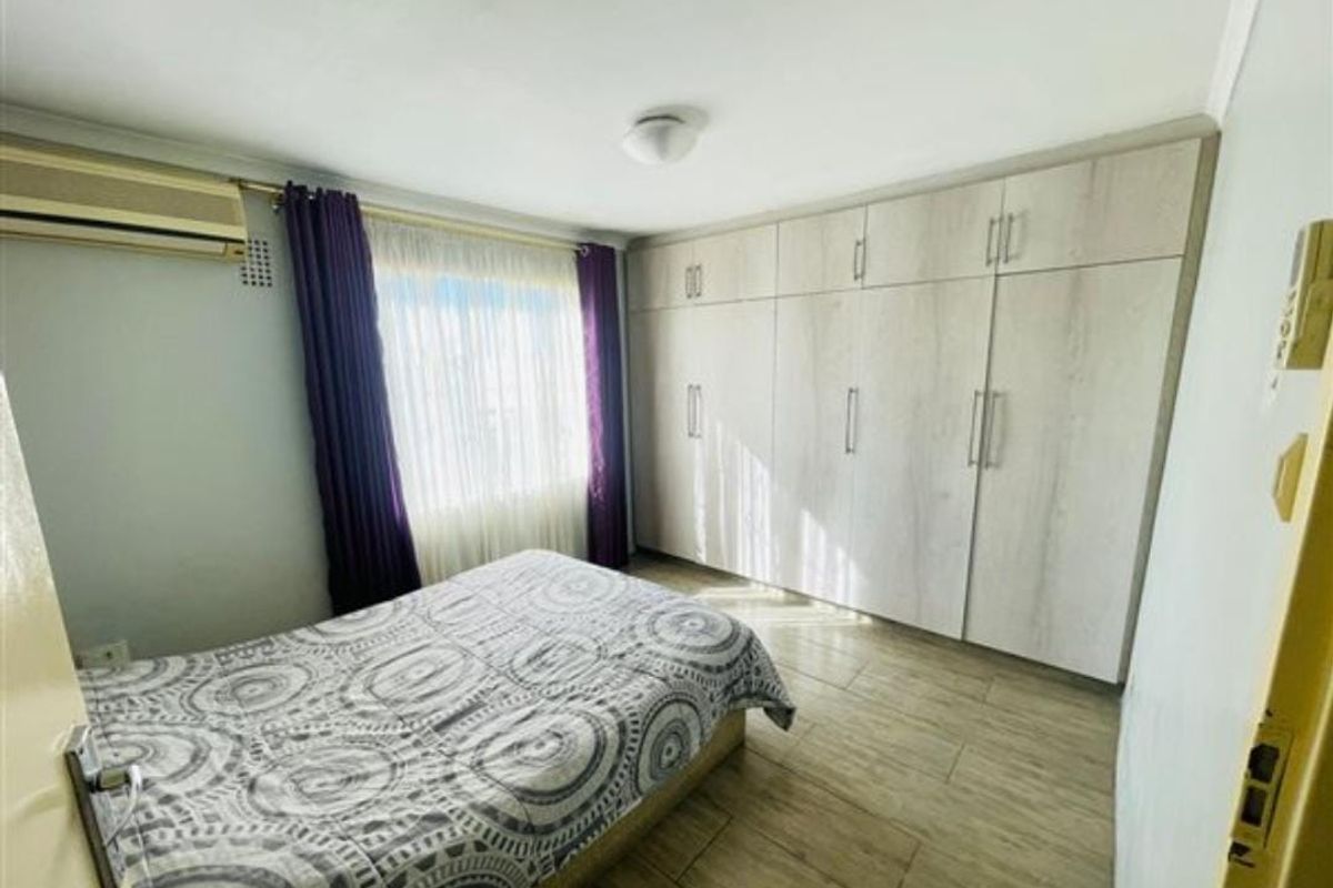 A well-maintained bedroom featuring extensive built-in cabinetry, tiled flooring, and a wall-mounted air conditioning unit.