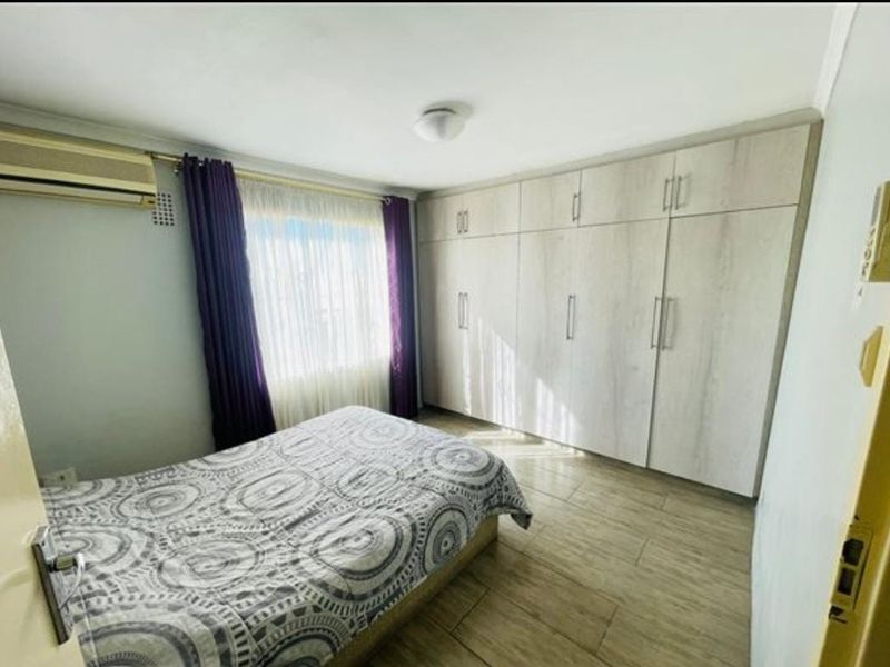 A well-maintained bedroom featuring extensive built-in cabinetry, tiled flooring, and a wall-mounted air conditioning unit.
