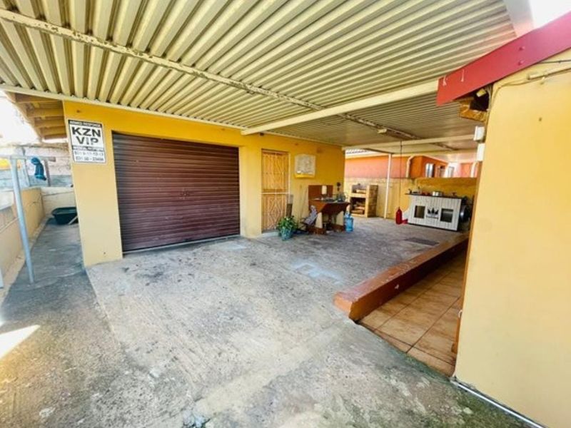 A covered outdoor patio area featuring concrete flooring, a roller shutter garage door, and a raised tiled platform, suitable for outdoor entertainment or utility use.