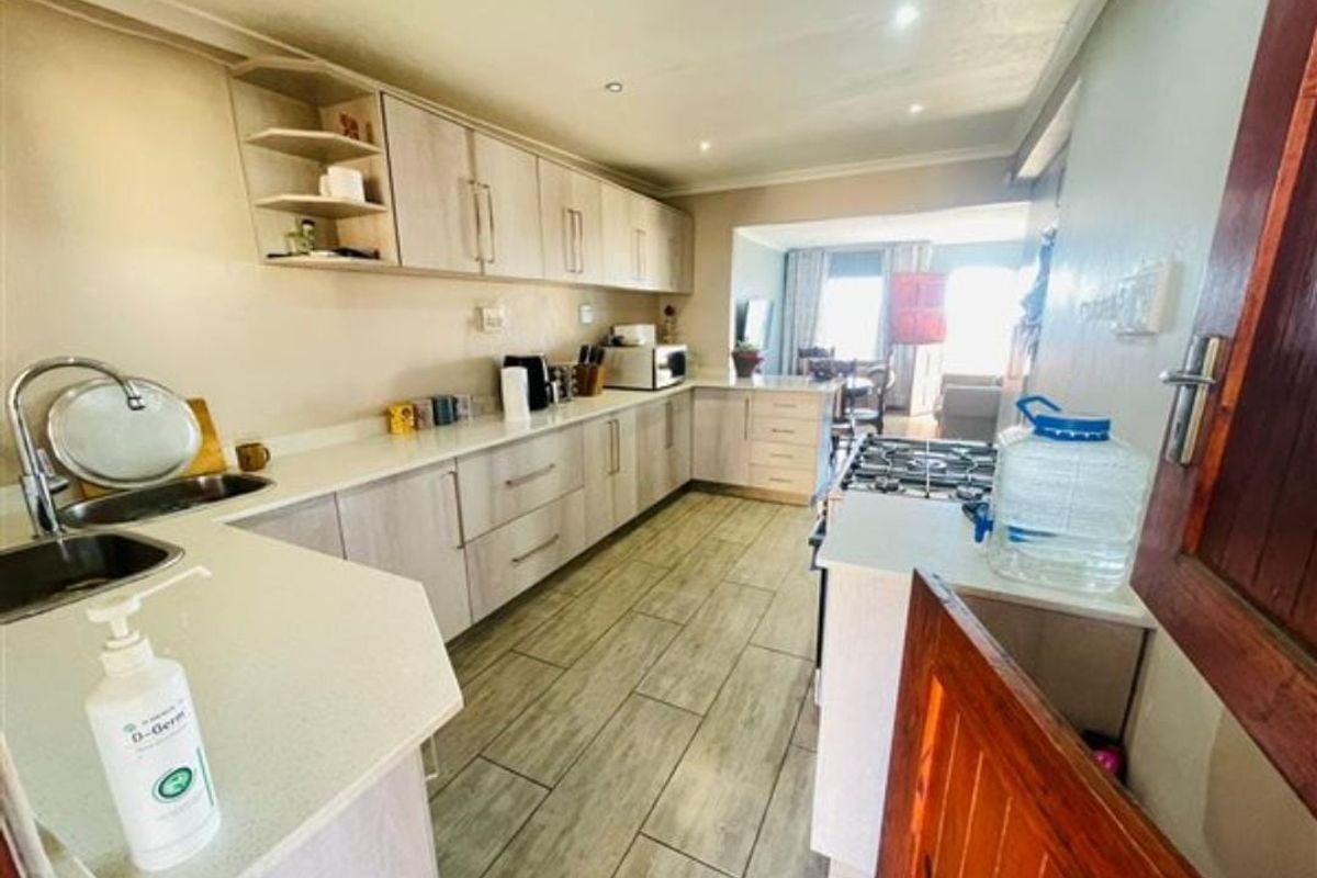 A functional kitchen featuring light-toned laminate cabinetry, stone countertops, a gas hob, and tiled flooring, with an open-plan layout leading to the living area.