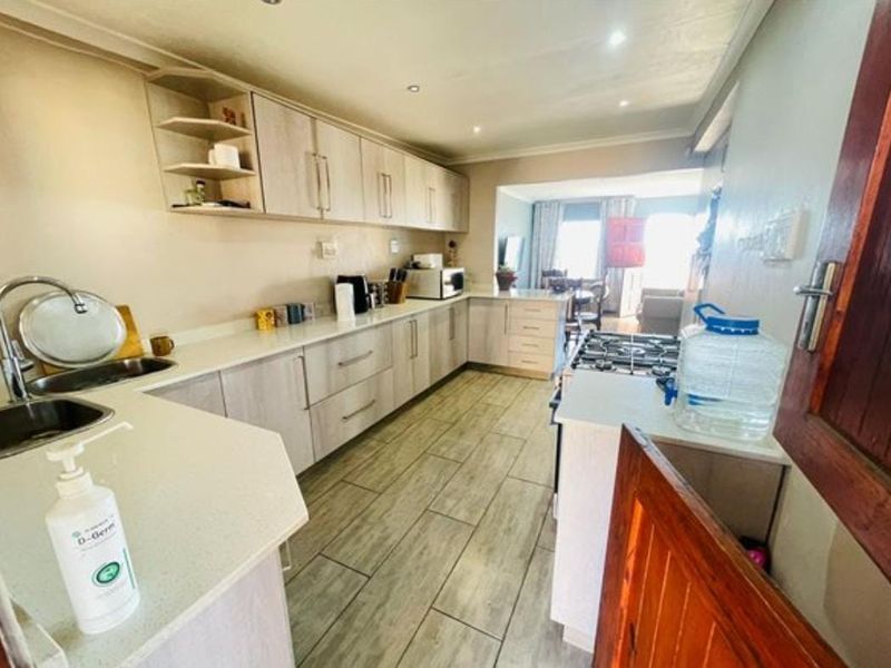 A functional kitchen featuring light-toned laminate cabinetry, stone countertops, a gas hob, and tiled flooring, with an open-plan layout leading to the living area.