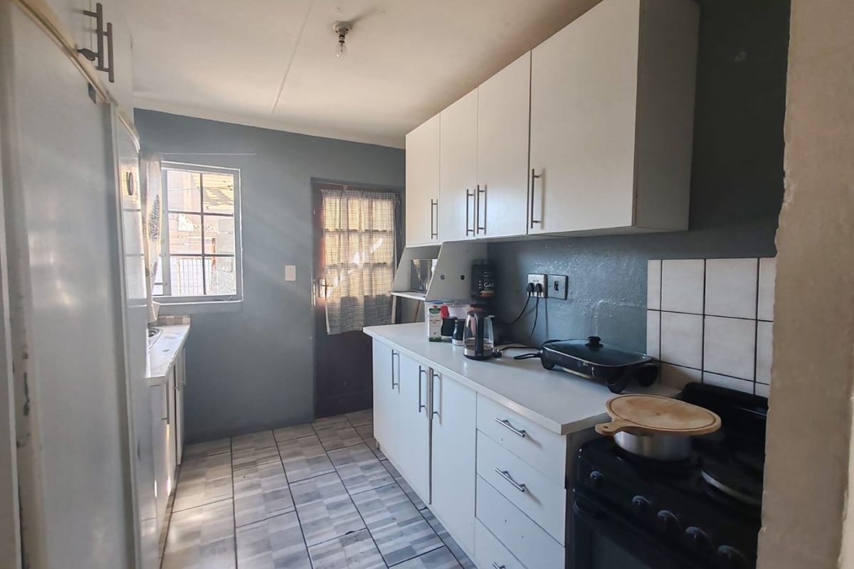 A functional kitchen featuring white cabinetry, tiled flooring, a tiled splashback, and a freestanding stove with direct access to the exterior.