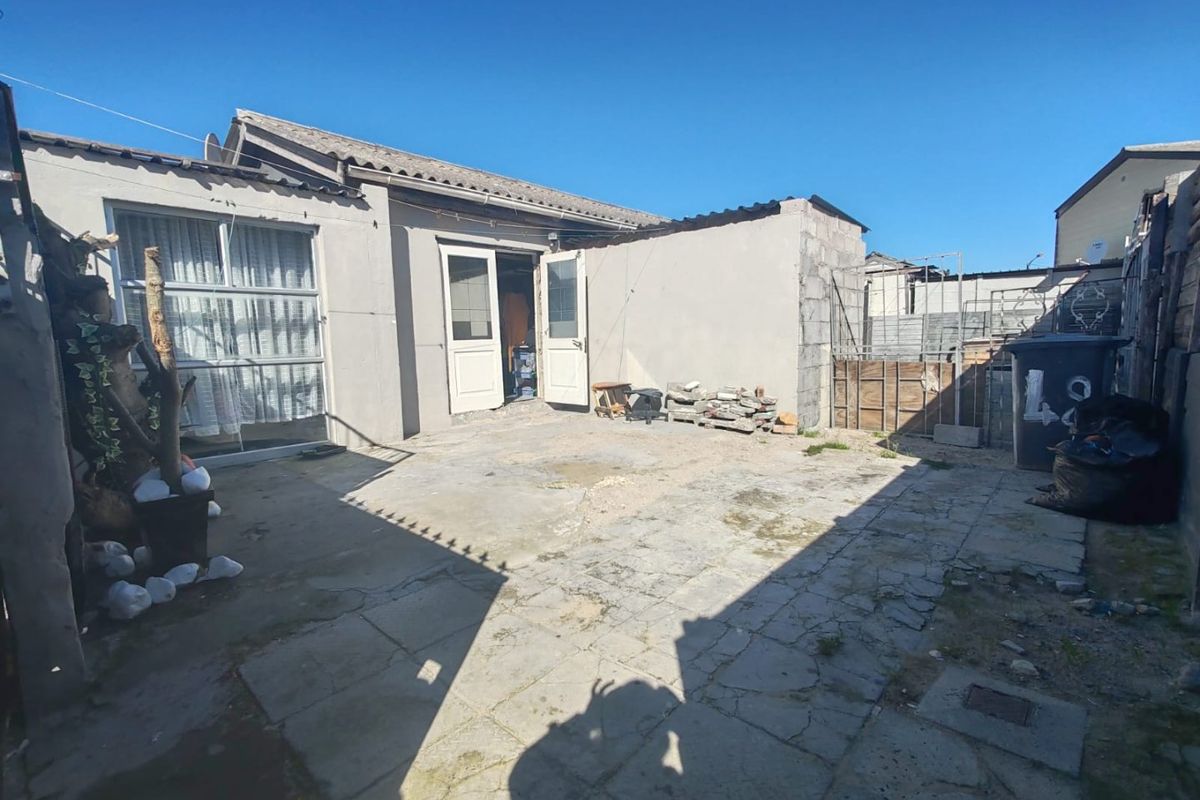 Rear exterior view of the property featuring a paved patio area, concrete block boundary walls, and access through double doors and a sliding glass door.