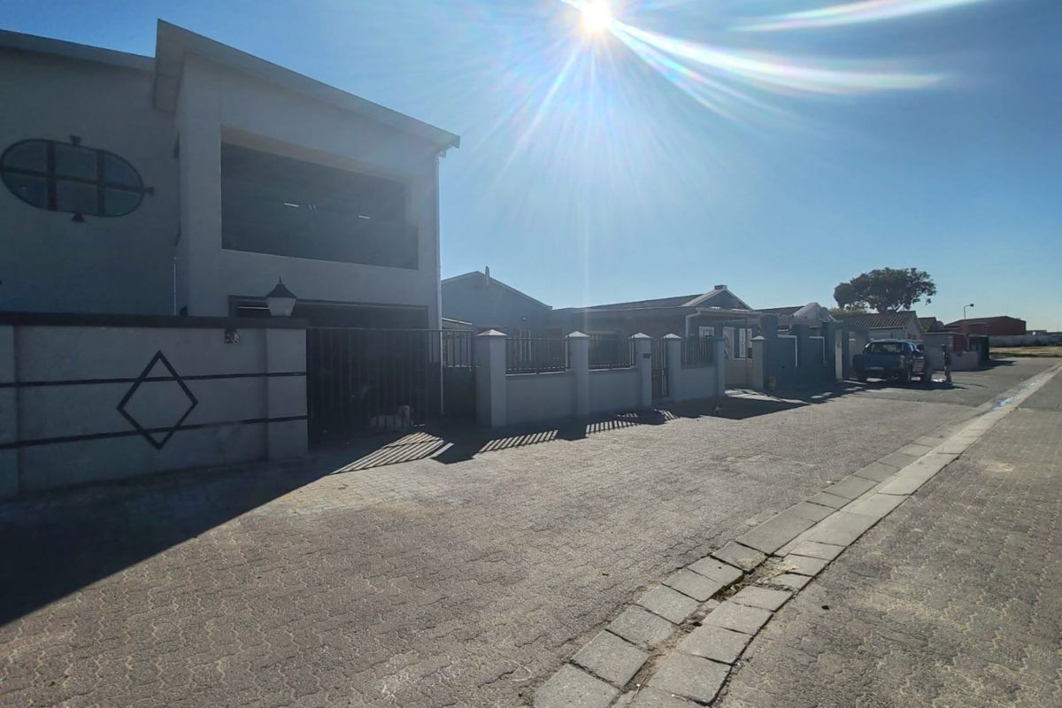Street view of the property showing the front facade, boundary wall, paved driveway, and upper-level balcony.