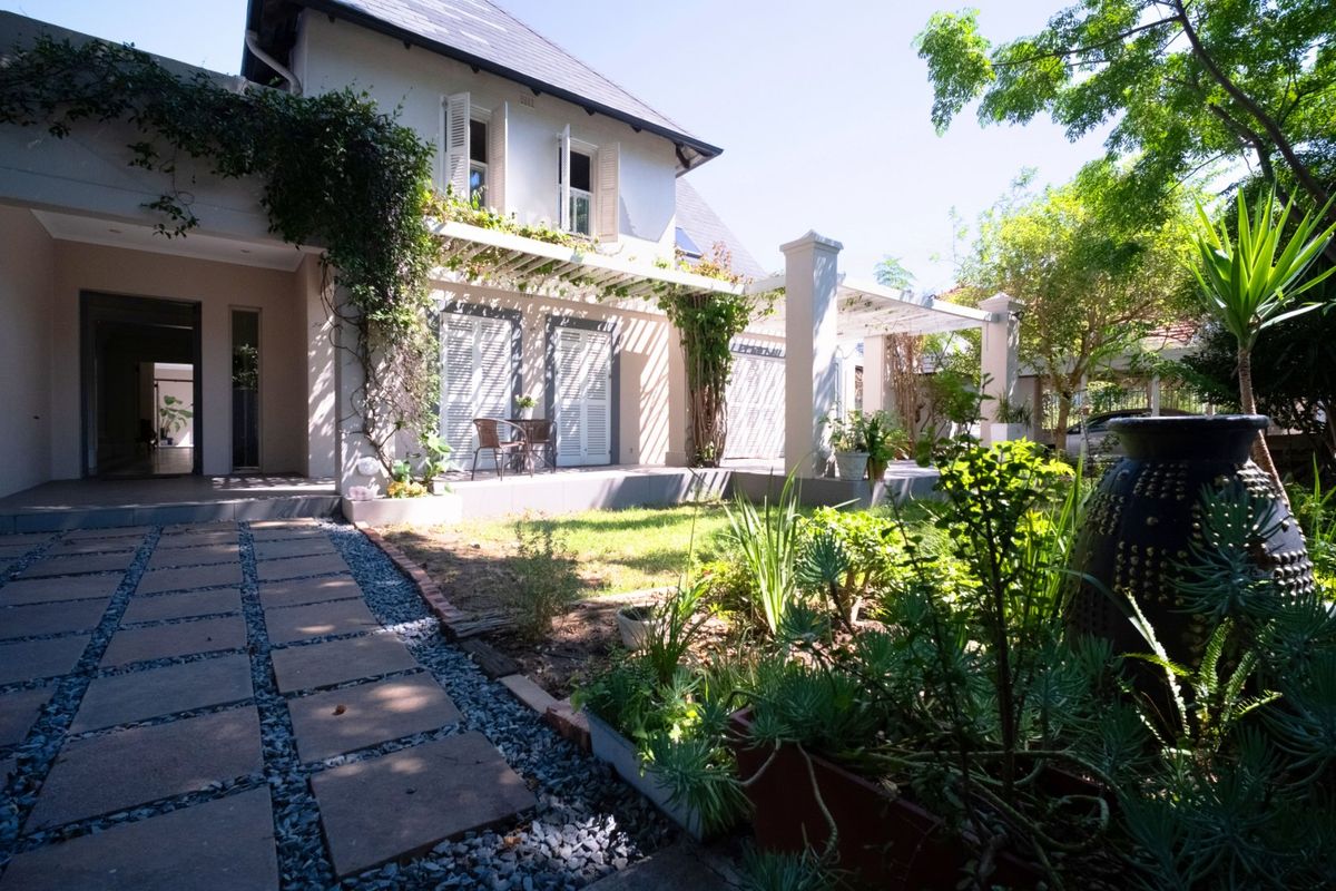 A well-maintained rear exterior featuring a covered patio with a pergola, shuttered windows, and a landscaped garden with a paved walkway.