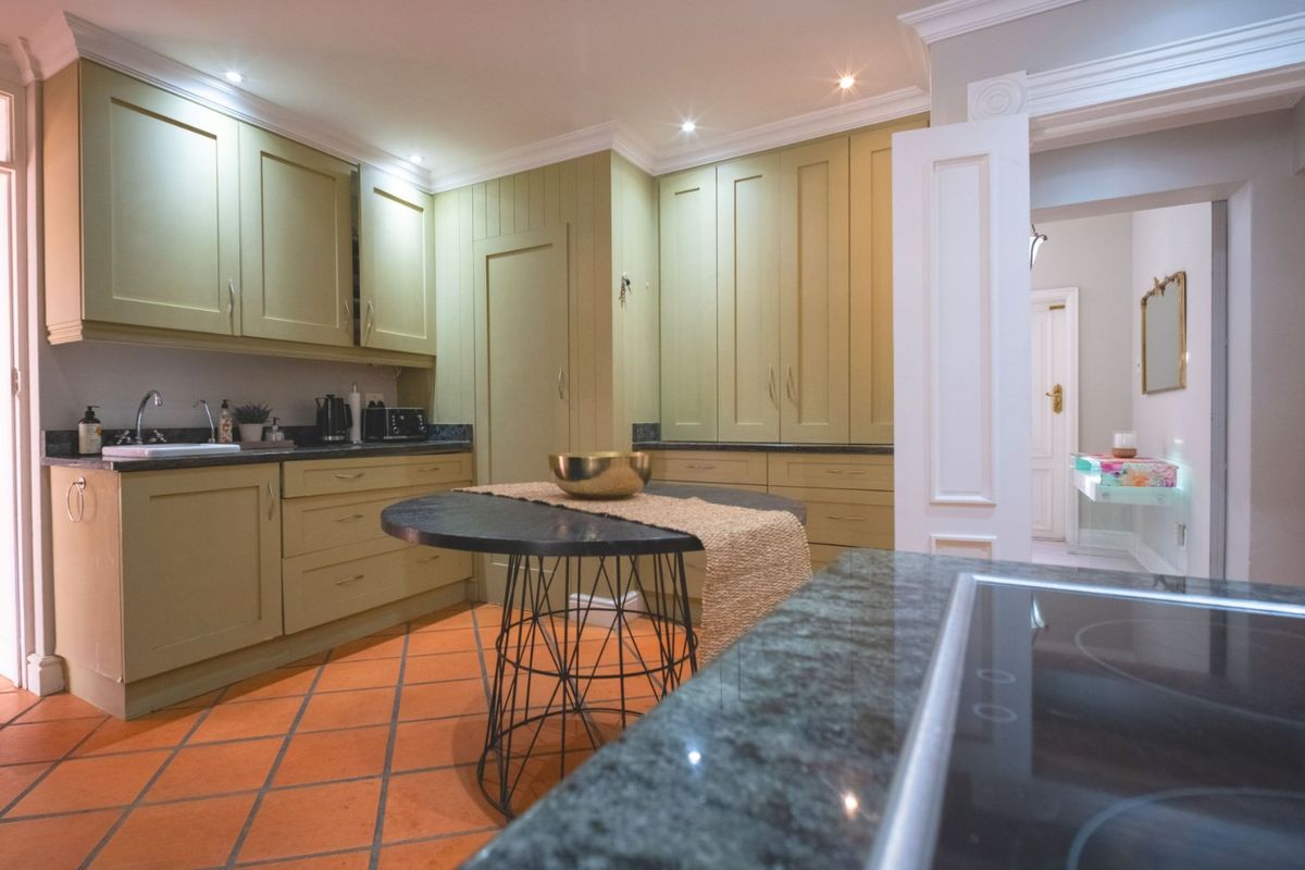A well-maintained kitchen featuring sage green cabinetry, granite countertops, recessed lighting, and terracotta tile flooring, offering a classic and functional culinary space.