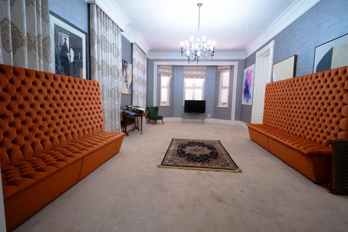 A spacious living room featuring elegant crown molding, a central chandelier, recessed lighting, and large bay windows with textured wall finishes.