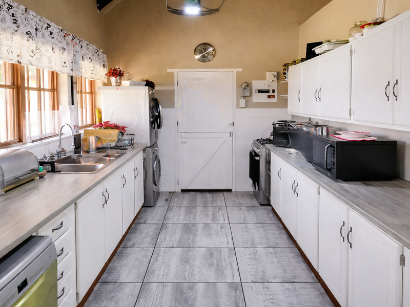 Functional kitchen featuring white cabinetry, laminate countertops, tiled flooring, and a stable door, providing a practical workspace with integrated appliances.