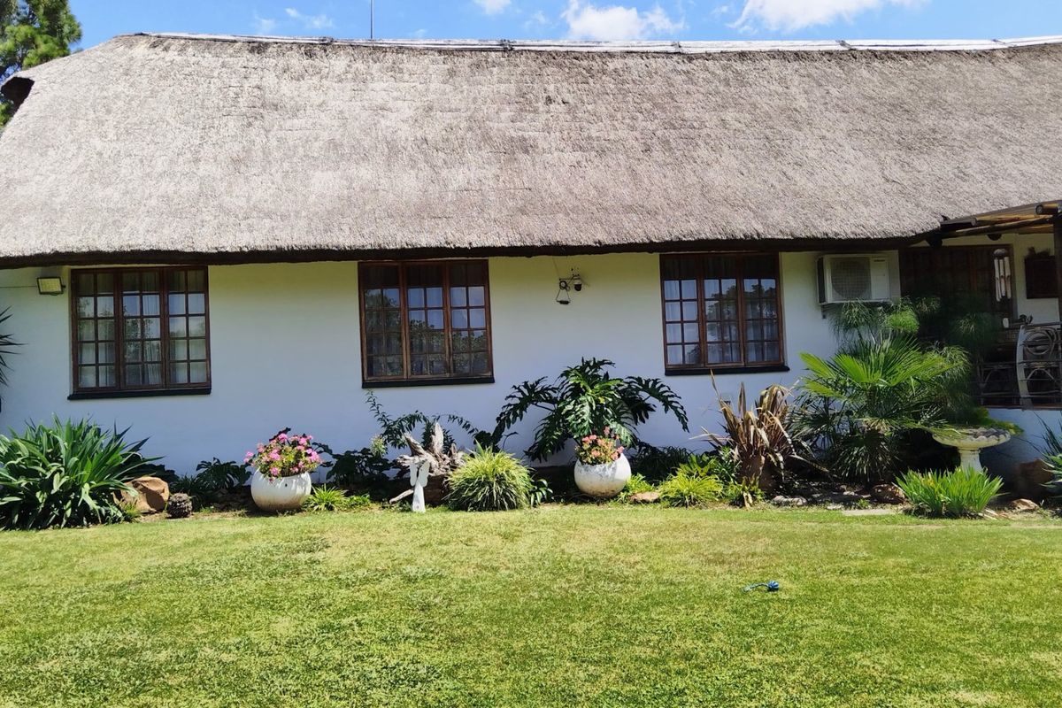 Rear view of a house featuring a traditional thatch roof, timber-framed windows, and an exterior air conditioning unit set against a landscaped garden.
