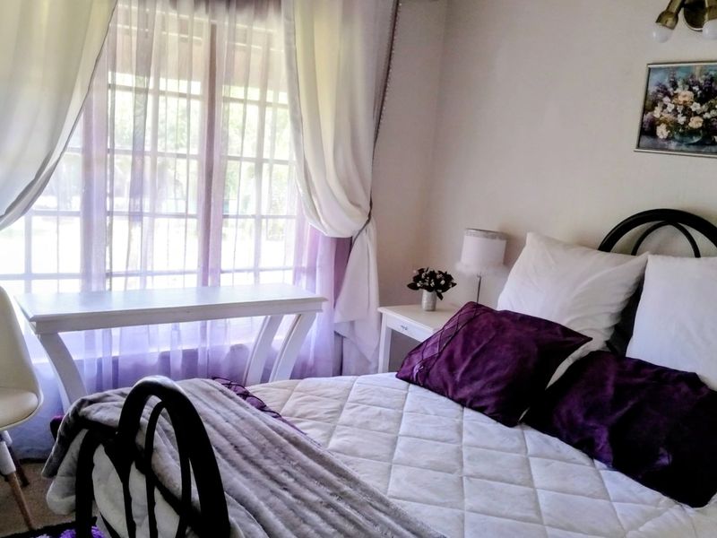A cozy bedroom featuring a window with natural light and a wall-mounted light fixture.