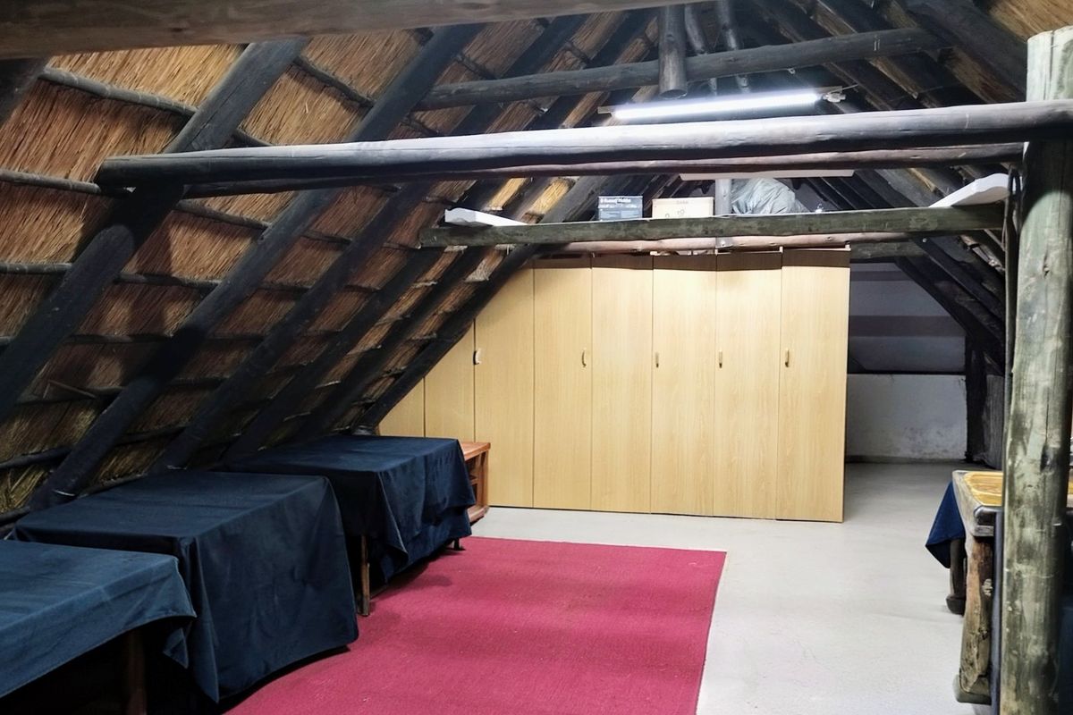 Attic-style bedroom featuring exposed timber rafters, a traditional thatched roof, and extensive built-in wooden cabinetry for storage.
