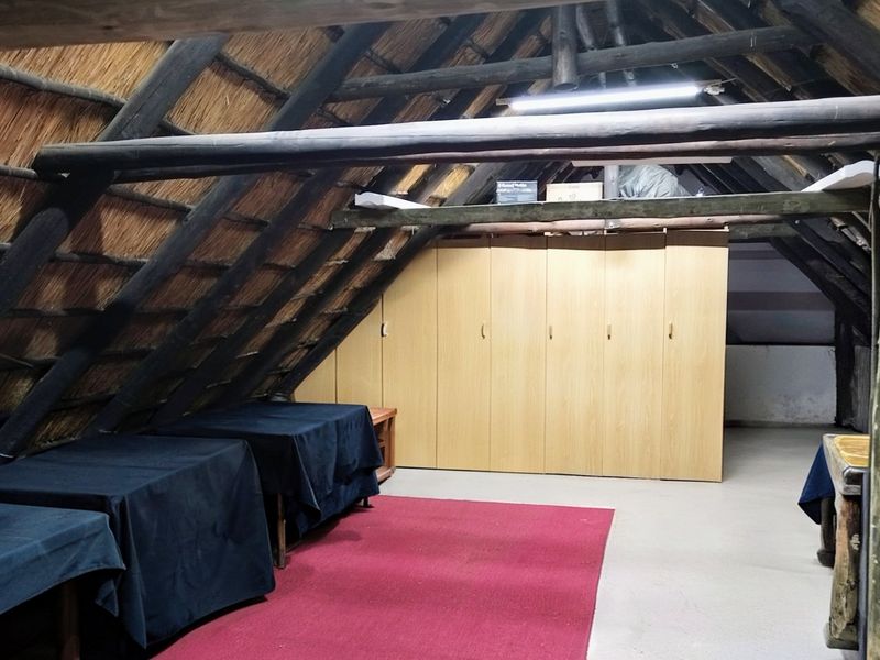 Attic-style bedroom featuring exposed timber rafters, a traditional thatched roof, and extensive built-in wooden cabinetry for storage.