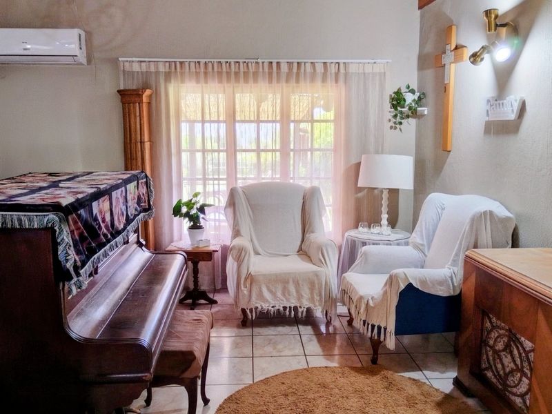 A cozy living room featuring tiled flooring, a wall-mounted air conditioning unit, and large french doors allowing natural light into the space.