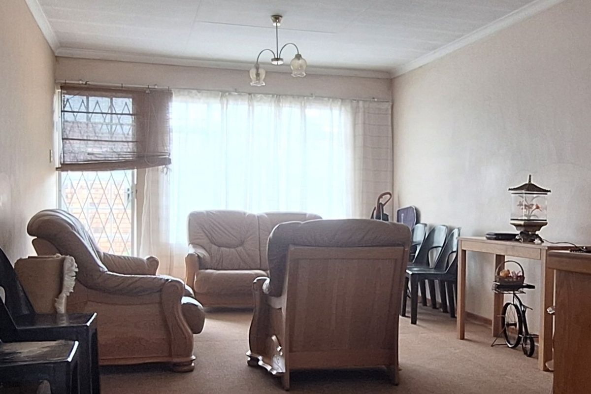 A living room area featuring carpet flooring, ceiling cornices, and a security gate leading to the exterior.