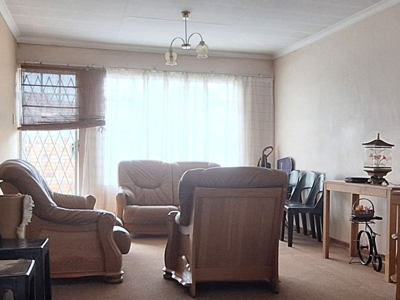 A living room area featuring carpet flooring, ceiling cornices, and a security gate leading to the exterior.