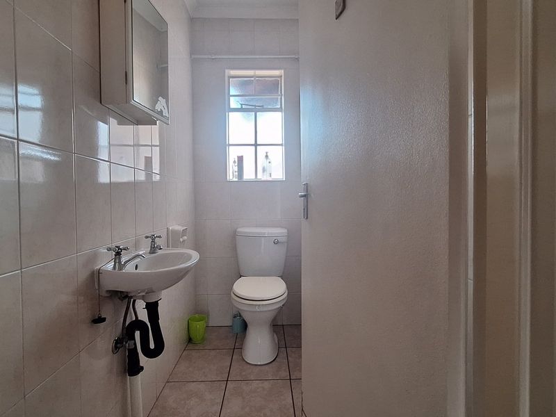 A compact bathroom featuring a wall-mounted basin, toilet, and tiled finishes throughout, offering a functional and clean space.