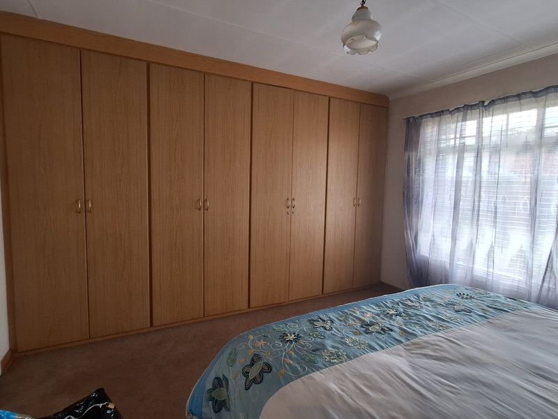 A bedroom featuring extensive wall-to-wall built-in wooden cupboards, carpeted flooring, and natural light through a large window.