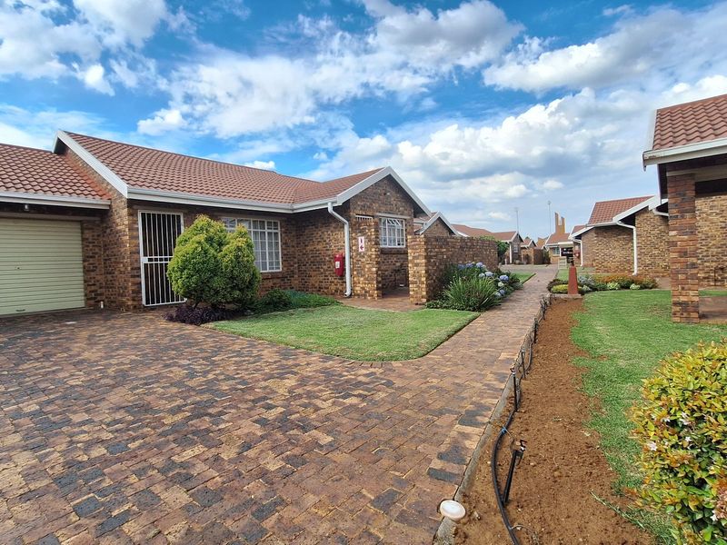 A well-maintained face brick townhouse featuring a paved driveway, single garage, and neat front garden with a paved walkway.