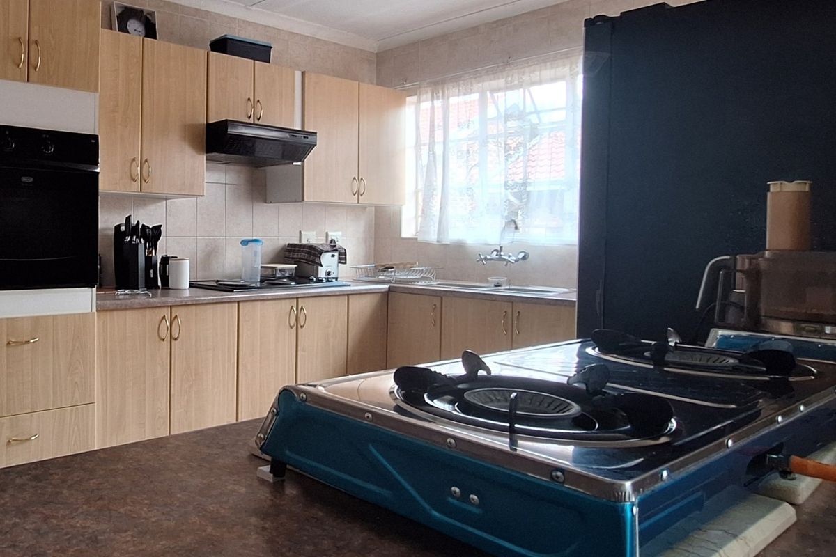 A functional kitchen featuring light wood-finish cabinetry, tiled backsplash, built-in oven, extractor fan, and ample counter space with a double sink.