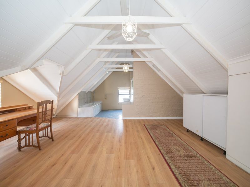 Spacious attic-style bedroom featuring vaulted ceilings with exposed rafters, laminate flooring, an integrated bathtub, and built-in storage solutions.
